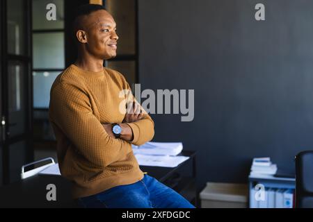 Selbstbewusster Geschäftsmann, der mit gekreuzten Armen in moderner Büroumgebung steht, Kopierraum Stockfoto