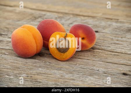 Ein Haufen reifer Aprikosen und eine in zwei Hälften geschnitten, um den saftigen Innenraum, rustikalen Holztisch zu präsentieren Stockfoto