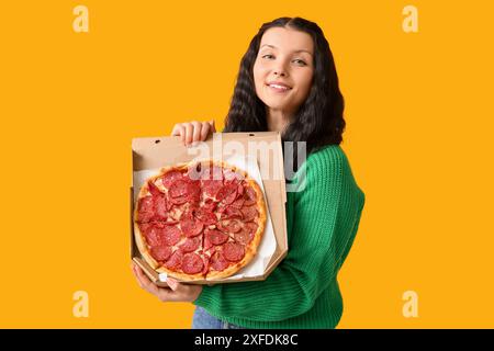 Schöne junge Frau, die Pappschachtel mit leckerer Pizza auf gelbem Hintergrund hält Stockfoto