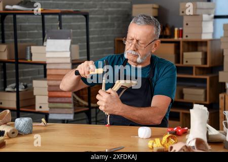 Reifer Schuhmacher repariert gebrochene Ferse am Tisch in der Werkstatt Stockfoto