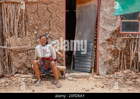 Dorf afrikanische Frau Huckepack trägt Kind im Rücken, Schlammhaus im Hintergrund Stockfoto