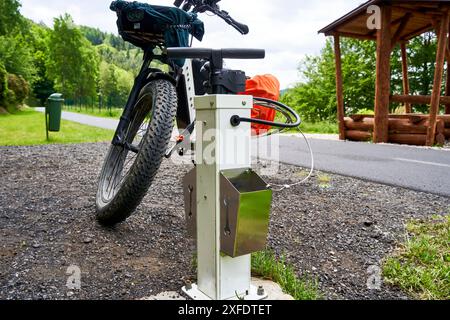 E-Fatbike an einer kostenlosen Tankstelle mit Luftpumpe und Werkzeugen für Radfahrer im tschechischen Erzgebirge neben einer rustikalen Raststätte Stockfoto