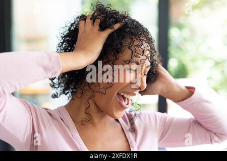 Frustrierte Frau, die den Kopf mit den Händen hält und in der häuslichen Umgebung schreiend Stockfoto