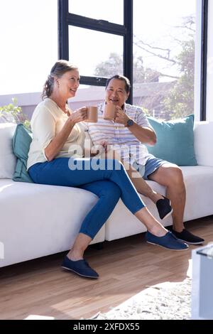 Entspannen Sie auf der Couch, ein älteres Paar genießt Kaffee und lächelt zusammen Stockfoto