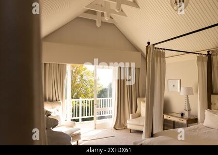 Helles Schlafzimmer mit Himmelbett und gemütlichem Sitzbereich in der Nähe eines großen Fensters, Kopierbereich Stockfoto
