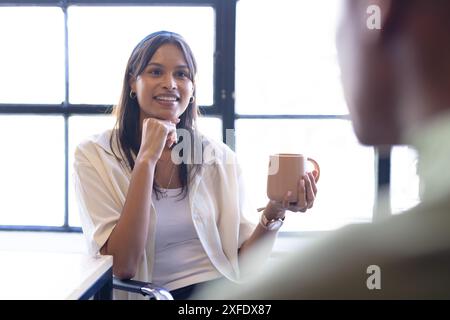 Eine Kaffeetasse hält, eine Frau, die sich mit einem Kollegen im Büro unterhält Stockfoto