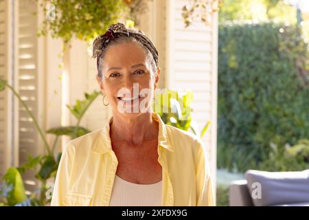 Lächelnde reife Frau, die zu Hause steht und den sonnigen Tag im Garten genießt Stockfoto