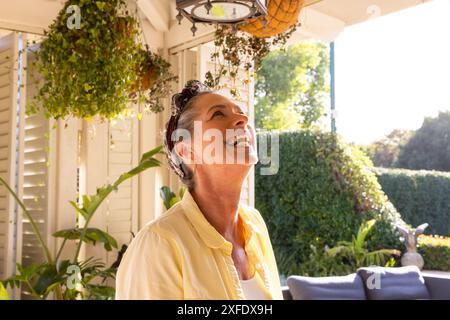 Lächelnde reife Frau genießt den sonnigen Tag auf der gemütlichen Gartenterrasse Stockfoto