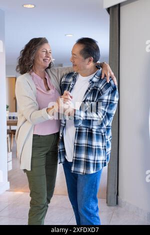 Lächelndes Seniorenpaar tanzt zusammen im Wohnzimmer und genießt die Urlaubszeit Stockfoto