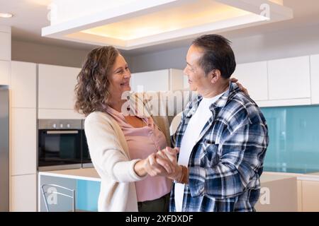 Seniorenpaar tanzt zusammen in der modernen Küche und genießt die Urlaubszeit Stockfoto