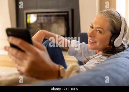Musik über Kopfhörer hören, reife Frau entspannen und Smartphone verwenden Stockfoto