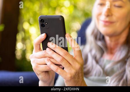 Mit dem Smartphone lächelt die reife Frau zu Hause und entspannt sich Stockfoto
