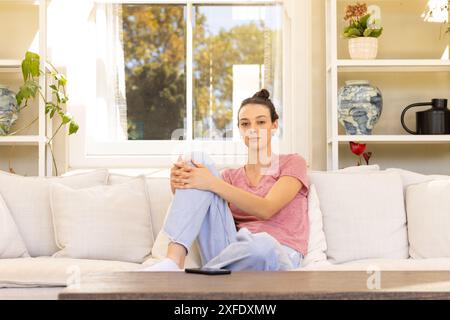 Auf der Couch sitzend, eine junge Frau, die sich zu Hause in lässiger Kleidung entspannt Stockfoto