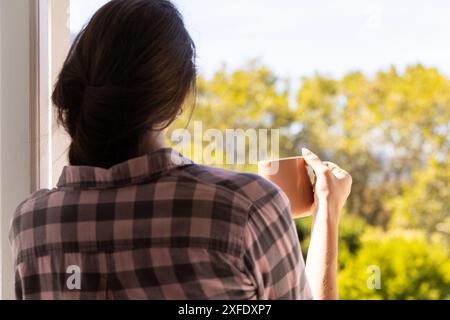 Die Frau hält eine Kaffeetasse und genießt vom Balkon einen ruhigen Blick auf den Morgen Stockfoto