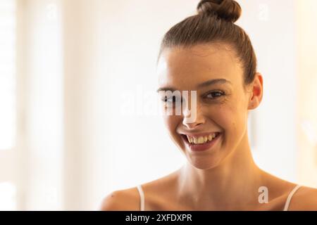 Lächelnde junge Frau zu Hause, die in die Kamera mit natürlichem Licht blickt Stockfoto