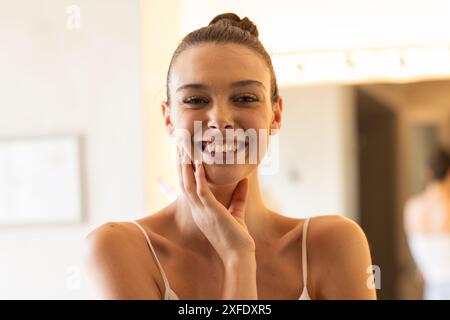 Lächelnde junge Frau, die das Gesicht berührt, die Morgenroutine zu Hause genießt Stockfoto