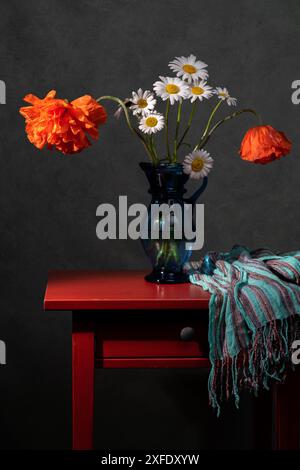 Blumenstrauß aus rotem Mohn und weißen Gänseblümchen in einer blauen Vase auf dem Tisch. Grauer Hintergrund. Stockfoto