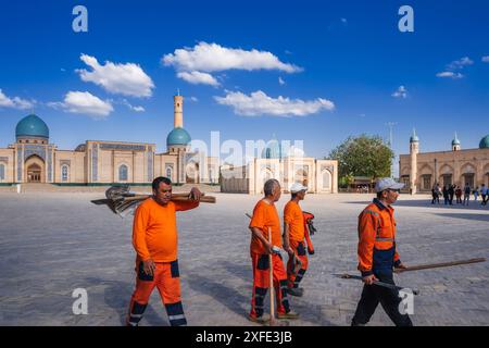 Gruppe usbekischer männlicher Hausmeister in orangen Uniformen mit Schaufeln auf der Straße im Frühling auf dem Platz des Hazrati Imam Architekturkomplexes. Taschkent, Usbekistan - 17. April 2024 Stockfoto