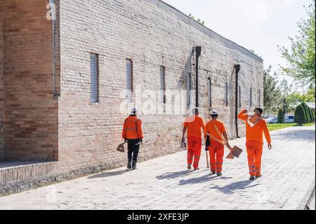 Gruppe usbekischer männlicher Hausmeister in orangen Uniformen mit Schaufeln im Sommer auf der Straße in Taschkent in Usbekistan Stockfoto