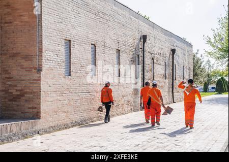 Gruppe von usbekischen männlichen Hausmeister in orange Uniformen mit Schaufeln vor Barak Khan Madrasah im Frühjahr. Taschkent, Usbekistan - 17. April 2024 Stockfoto