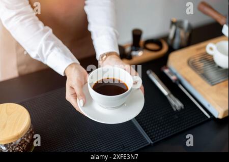 Ein Nahaufnahme einer Barista, die eine Kaffeetasse über einer Theke hält und in einem Café arbeitet. Service, Kleinunternehmen, Teilzeitjob Stockfoto