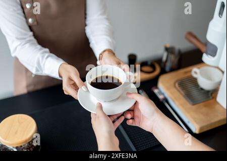 Ein Nahaufnahme eines weiblichen Barista, der einer Kundin eine Kaffeetasse über eine Theke gibt, die in einem Café arbeitet. Service, Kleinunternehmen, Teilzeit j Stockfoto