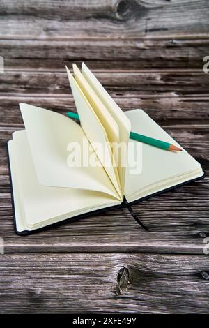 Offenes Notizbuch mit leeren Seiten und einem grünen Bleistift auf einem Holztisch. Stockfoto