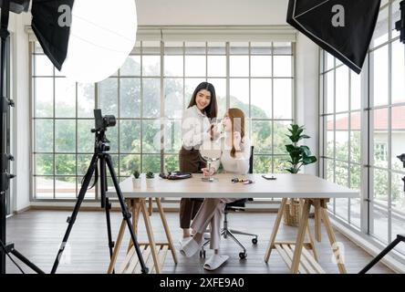 Zwei asiatische Frauen, die Inhalte für soziale Medien erstellen. Sie verwenden eine Studioeinrichtung, die eine auf einem Stativ montierte Kamera, Beleuchtungsausrüstung und einen VAR umfasst Stockfoto