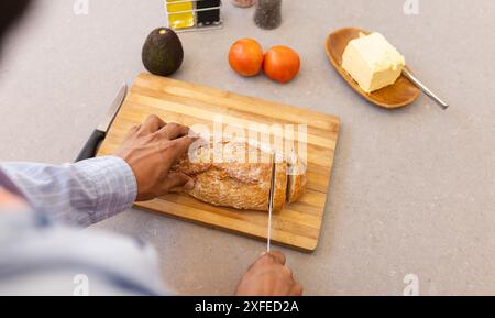 Brot auf Holzbrett schneiden, Mann bereitet Zutaten mit Avocado und Tomaten zu Stockfoto