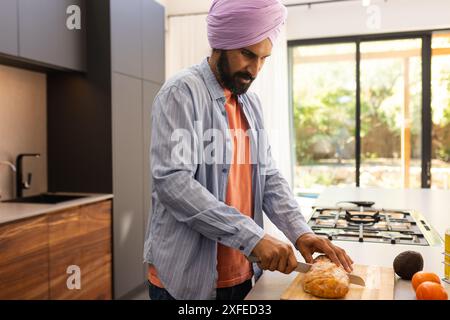 Brot auf Holzbrett schneiden, Mann, der Essen in moderner Küche zubereitet Stockfoto