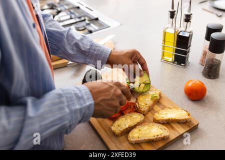 Avocadoscheiben, Mann, der Avocadotoast in moderner Küche mit frischen Zutaten zubereitet Stockfoto