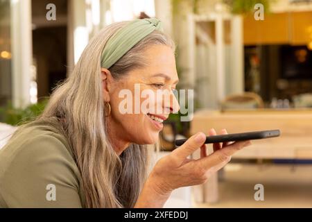 Lächelnde, reife Frau, die zu Hause per Smartphone Sprachnachrichten sendet und die Technologie genießt Stockfoto