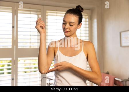 Lotion auf den Arm auftragen, junge Frau in weißem Tank-Top zu Hause Stockfoto