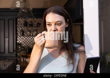 Kaffee trinken und Smartphone benutzen, junge Frau, die sich zu Hause entspannt Stockfoto
