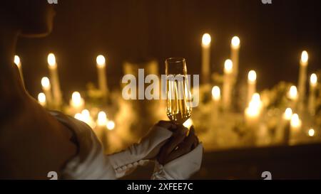 Nahaufnahme der Hand einer jungen Frau mit einem Glas Champagner an Weihnachten, beleuchtet von Weihnachtslichtern. In den Händen steht ein Glas Champagner gegen Stockfoto