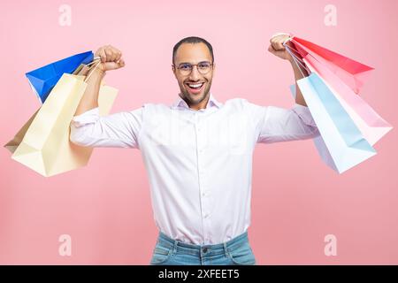 Starker glücklicher afroamerikanischer Mann, der Hemd und Brille trägt und Papiertüten zum Einkaufen hochhebt Stockfoto
