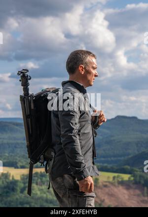 Der Fotograf steht auf der Spitze der Berge und hält einen Rucksack in der Hand mit einem Stativ für die Kamera. Sächsische Schweiz, Deutschland Stockfoto
