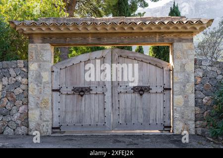 Halbrunde Holztore mit geschmiedeten Türgriffen und geschmiedeten Scharnieren. Eine Steinmauer vor dem Hintergrund majestätischer Berge. Mallorca, Spanien Stockfoto