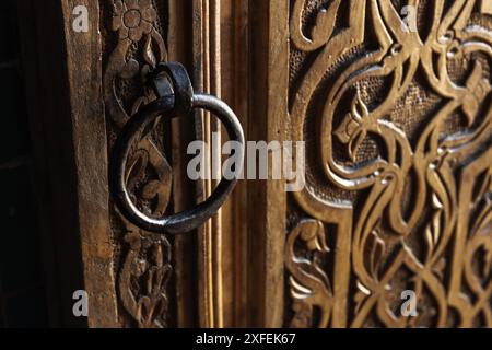 Runder Vintage-Griff an einer alten orientalischen Holztür, die mit geschnitzten Ornamenten verziert ist Stockfoto