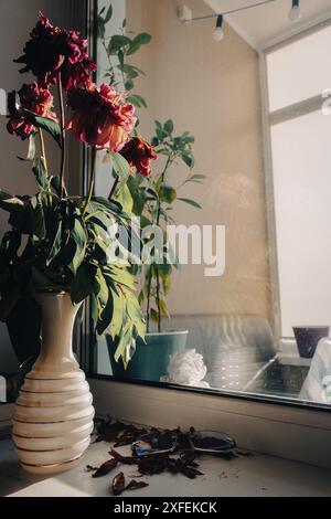 Verwelkter Blumenstrauß in Retro-Vase mit Brille auf Fensterbank. Verdorbene Pfingstrosenblüten im Zimmer. Wohnraum. Interieur im Retro-Stil. Das tägliche Leben. Stockfoto