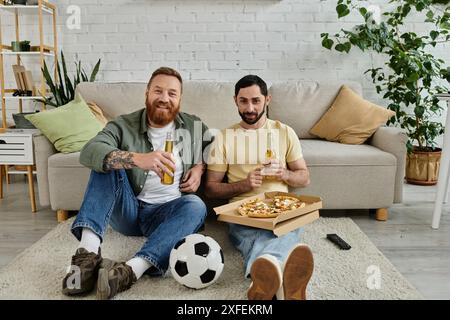 Zwei Männer, ein bärtiges schwules Paar, sitzen auf dem Boden und genießen Pizza und Bier Stockfoto