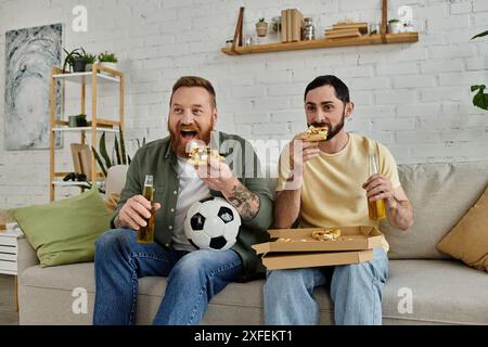 Zwei Männer mit Bärten sitzen auf einer Couch und genießen Pizza und Bier mit einem labrador Hund im Wohnzimmer. Stockfoto