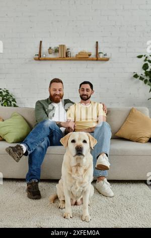 Zwei Männer mit Bärten verbrachten mit ihrem schwarzen labrador in gemütlicher Wohnzimmeratmosphäre schöne Zeit auf einer Couch. Stockfoto