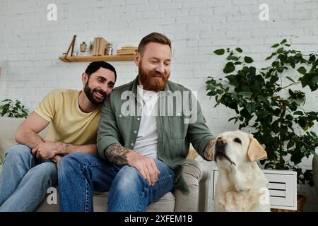 Zwei Männer, ein bärtiges schwules Paar, entspannen sich auf einer Couch mit ihrem labrador in einem gemütlichen Wohnzimmer. Stockfoto