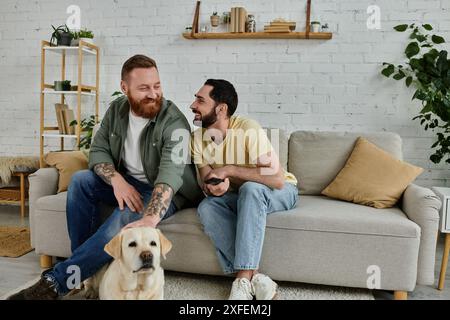 Zwei Männer, einer mit Bart, verbringen in einem gemütlichen Wohnzimmer mit einem Labrador auf einer Couch. Stockfoto