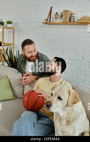 Bärtiger Mann entspannt sich auf der Couch mit Basketball, neben Labrador Hund, in gemütlicher Wohnzimmerumgebung. Stockfoto