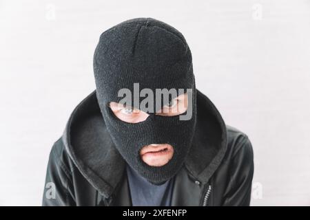 Ein Dieb in einer schwarzen Jacke. Ein Mann in einer schwarzen Balaklava mit einem bösen Gesichtsausdruck. Ein aggressiver Bandit auf weißem Hintergrund. Das Konzept von Stockfoto