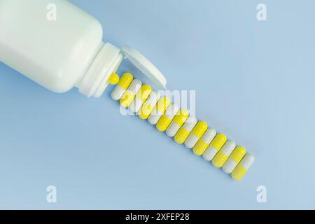Draufsicht der weißen Flasche mit den gelben Pillen auf blauem Hintergrund. Kopierbereich. Der Begriff Gesundheitsmedizin und Pharmazie. Herstellung der Medizin Stockfoto