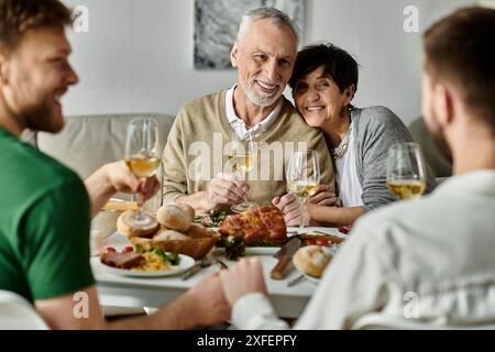 Ein schwules Paar teilt ein feierliches Abendessen mit ihren Familien, mit einem Lächeln und Weingläsern, die in einem Toast aufgerichtet werden. Stockfoto