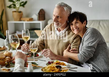 Fröhliche Eltern essen mit ihrem Sohn und seinem Partner bei einem gemütlichen Abendessen zu Hause. Stockfoto